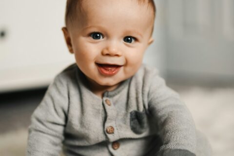 baby in gray sweater lying on white textile