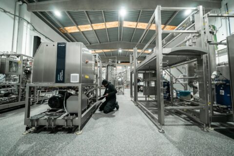 A worker repairs machinery in a factory setting.