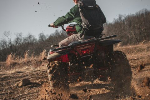 man riding red atv on brown field during daytime