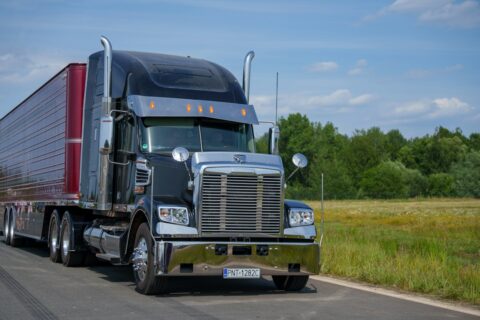 A black semi-truck drives down a rural road